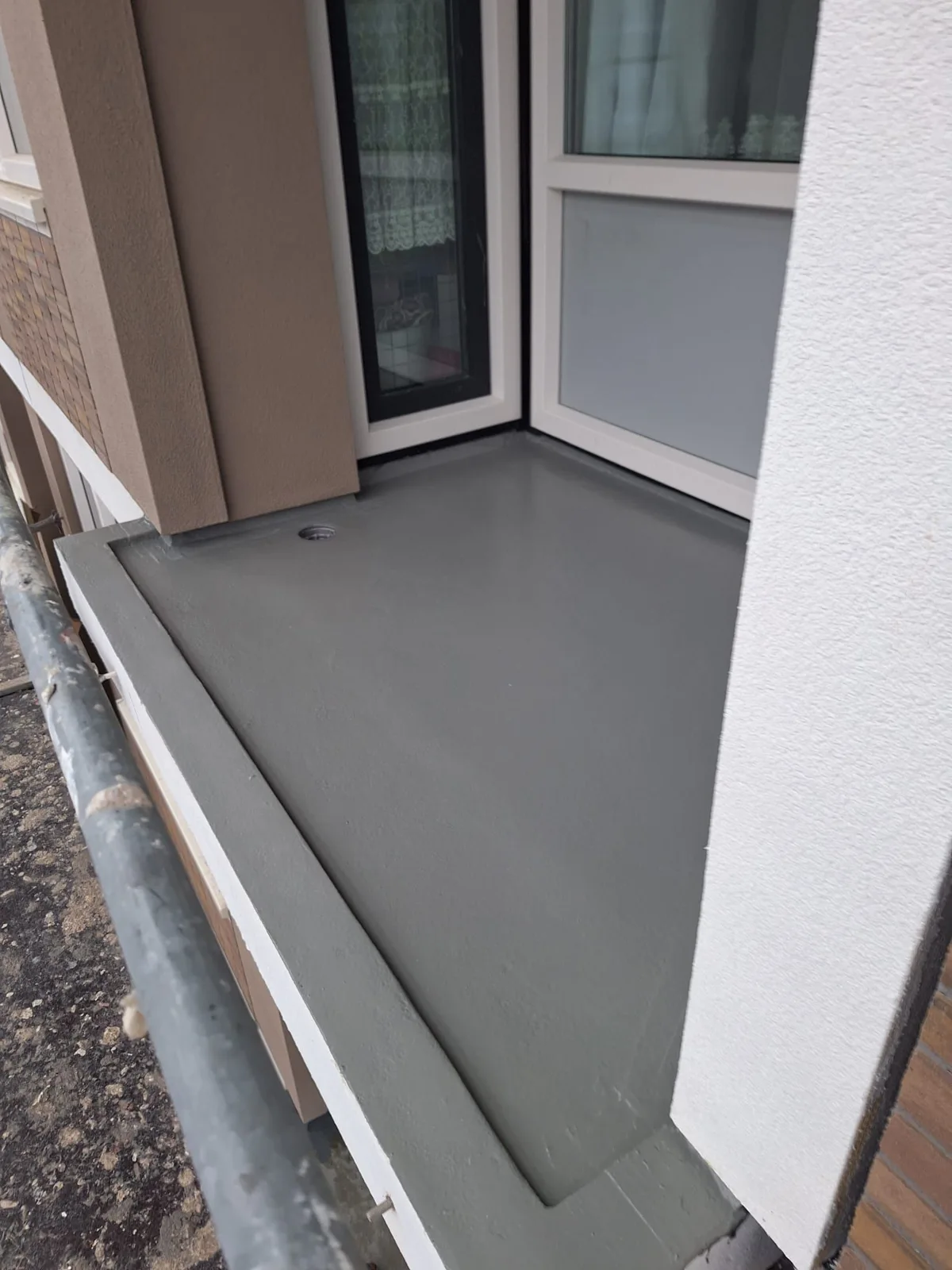 Grijs gecoat balkon met afgewerkte randen naast een glazen deur