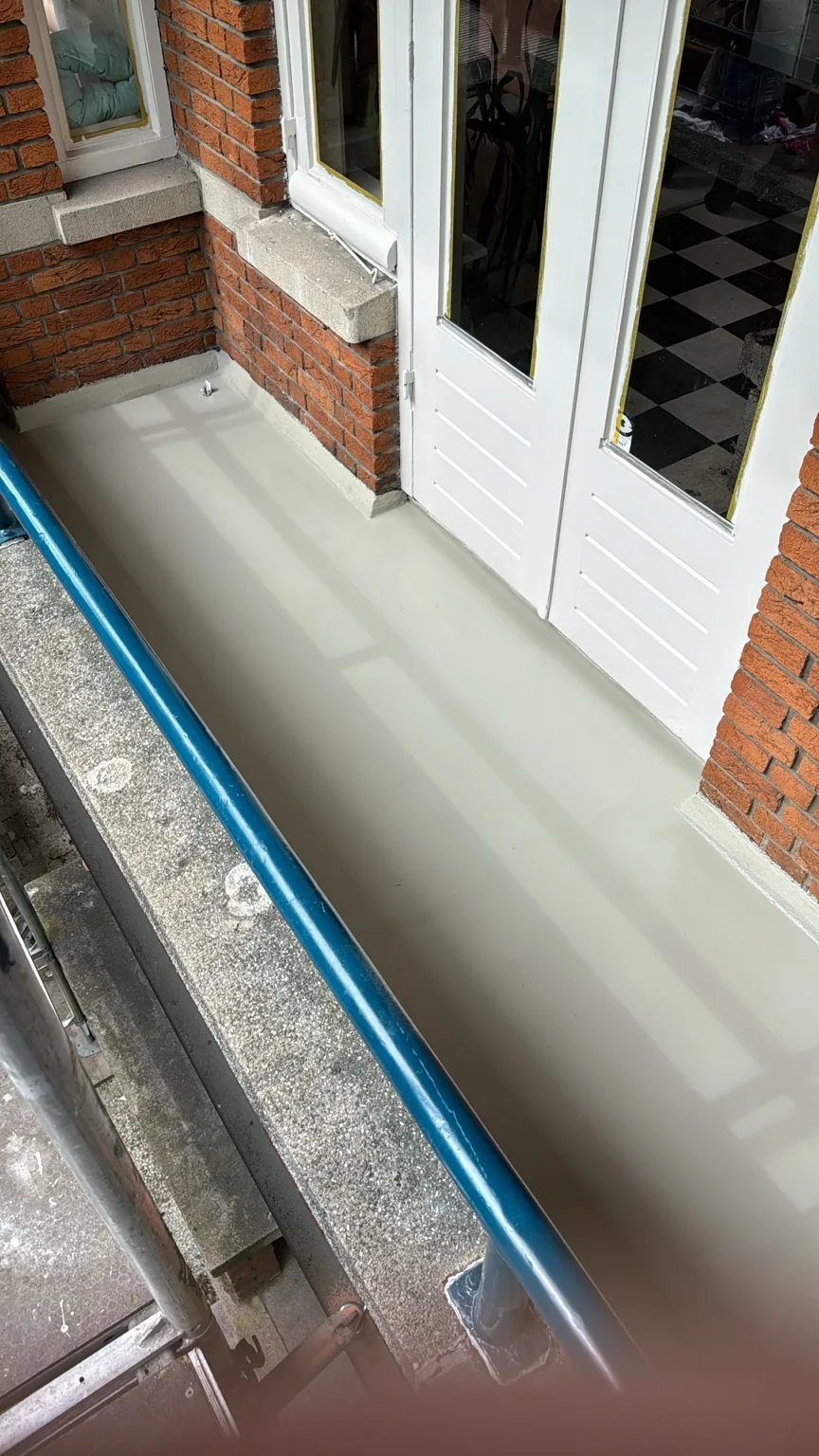 Balkonvloer met lichtgrijze coating langs witte deuren en gemetselde opstanden