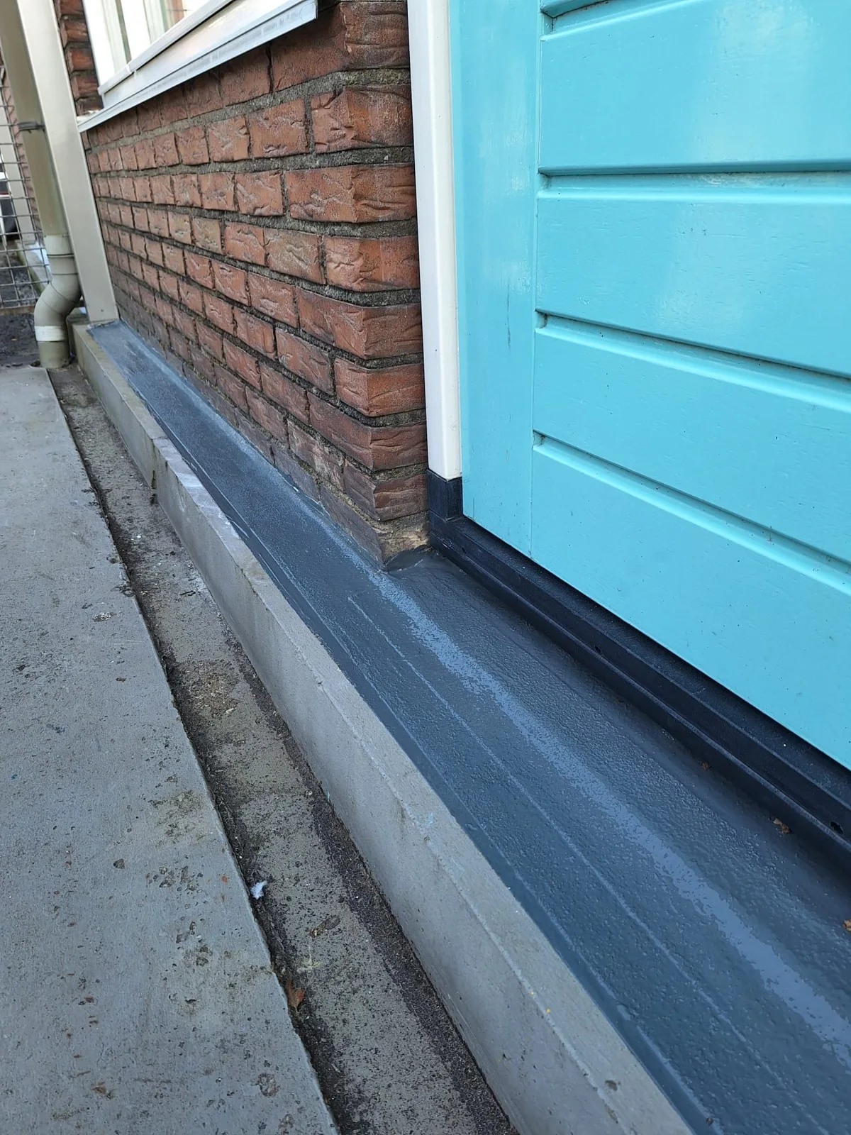 Afgewerkte grijze deurdorpel langs een blauwe deur en gemetselde gevel